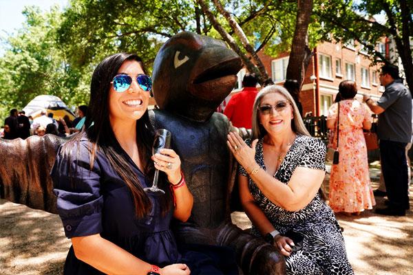 Two alumni showing their rings with Red mascot statue